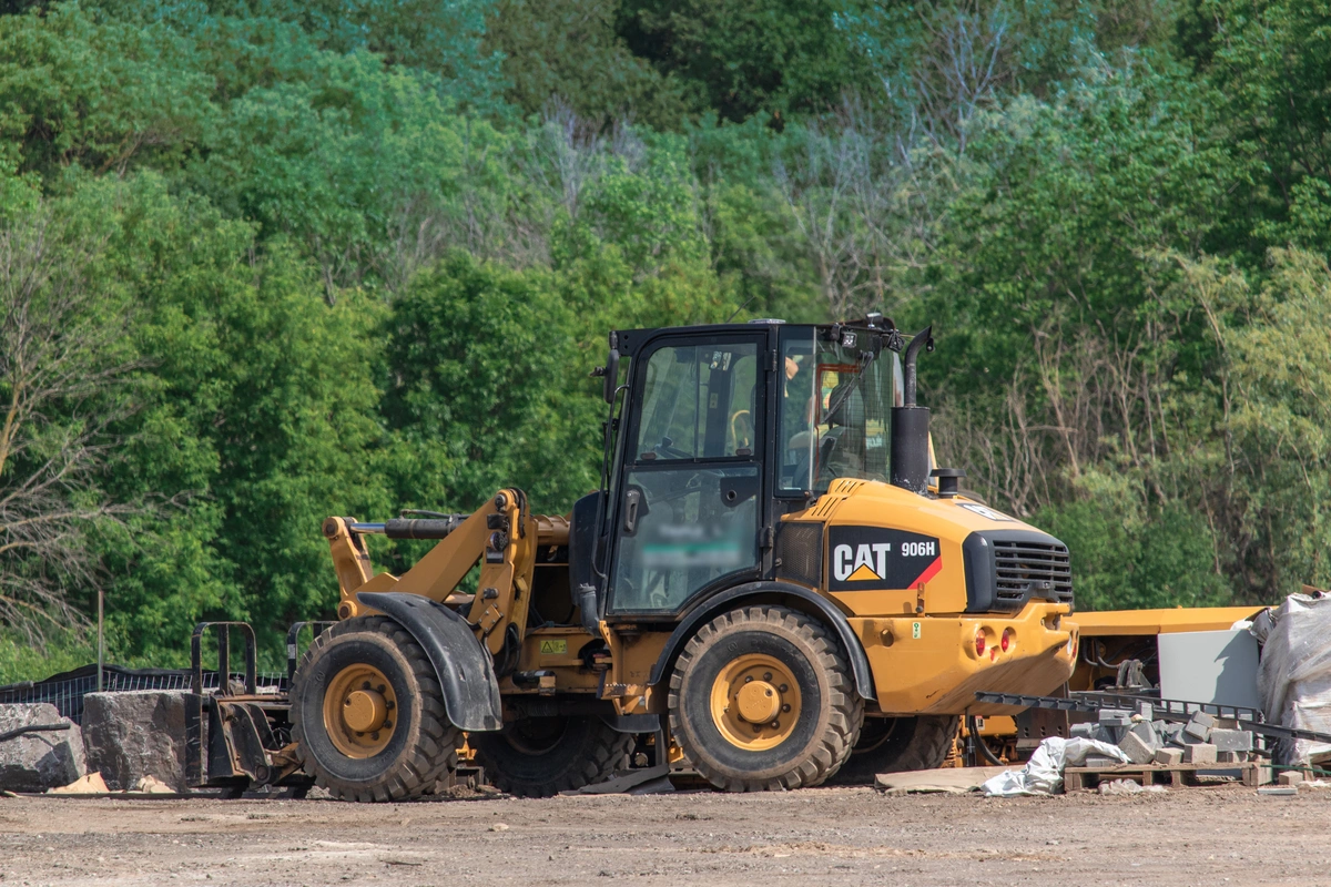 A yellow 906H Caterpillar wheel loader loader with fork attachments sitting idle