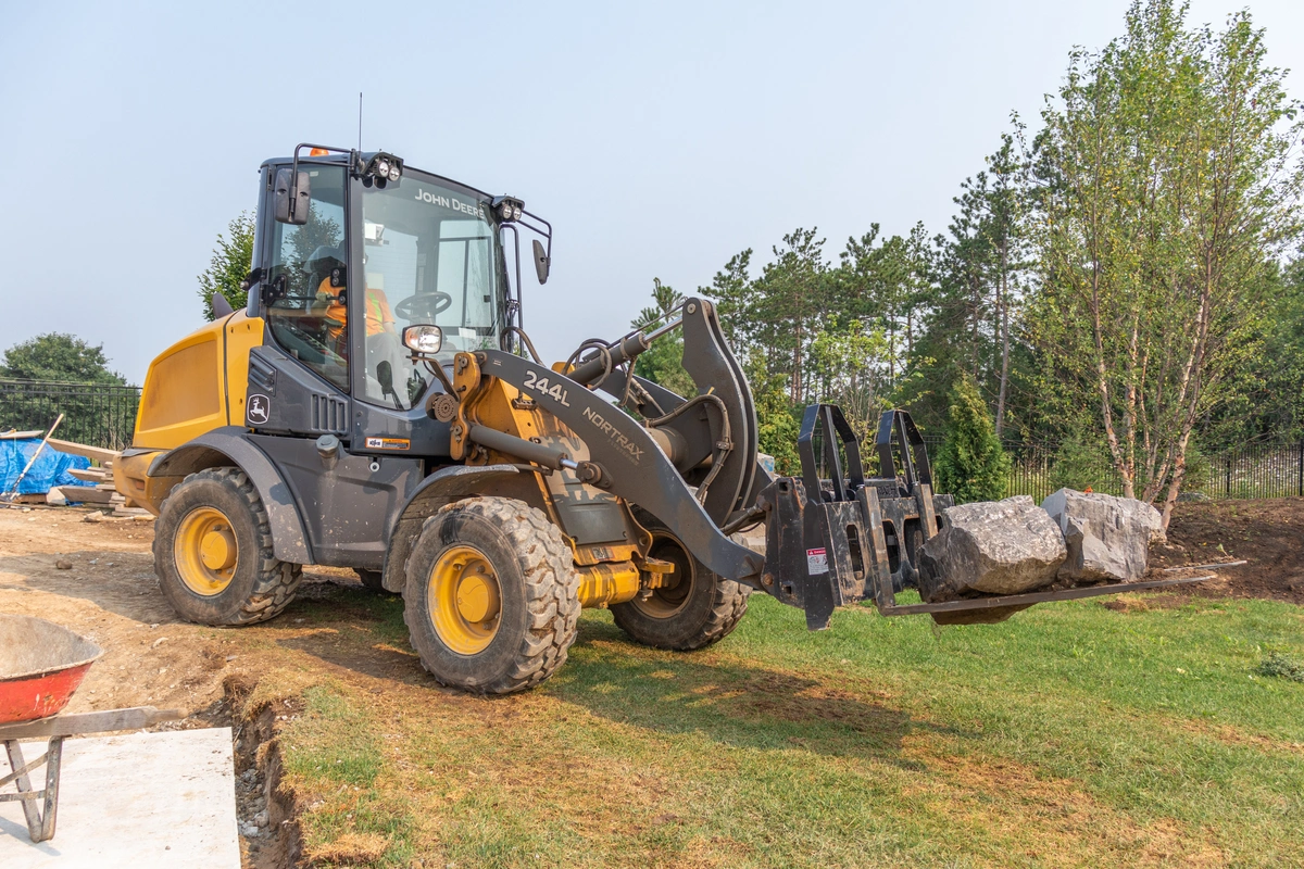 John Deere 244L compact wheel loader with fork pallets moving big rocks on a job site